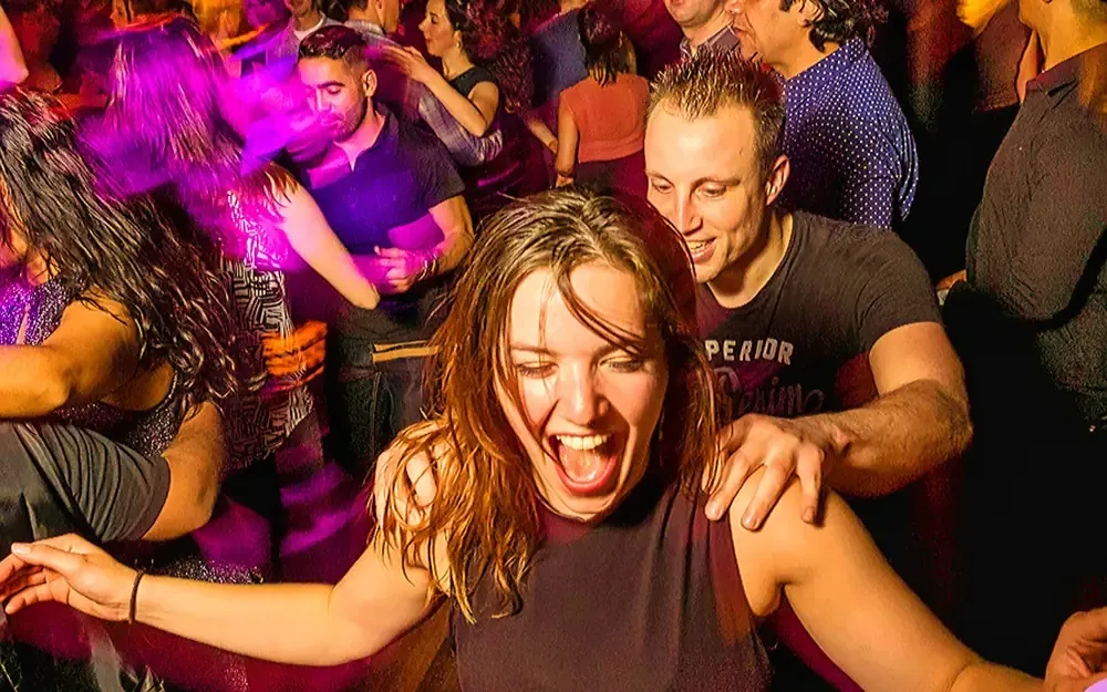 Joyful dancers on a packed salsa dance floor under colourful lights at Club Mystique in Amsterdam