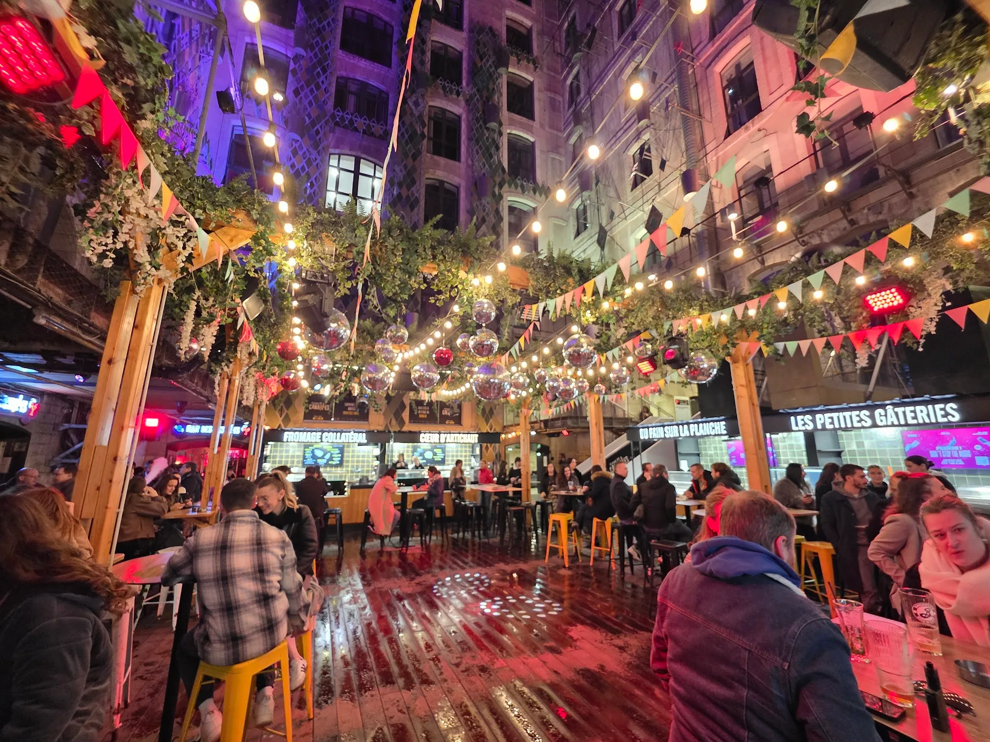 Evening outdoor crowd at La Place des Canailles with fairy lights and bunting decorations