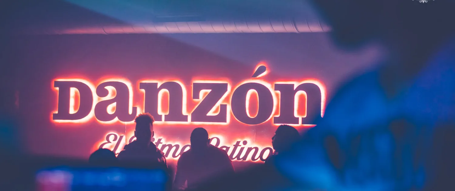 Glowing neon DANZÓN sign behind guests at the Vienna Latin club