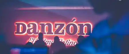 Glowing neon DANZÓN sign behind guests at the Vienna Latin club — bachata, salsa venue in Vienna