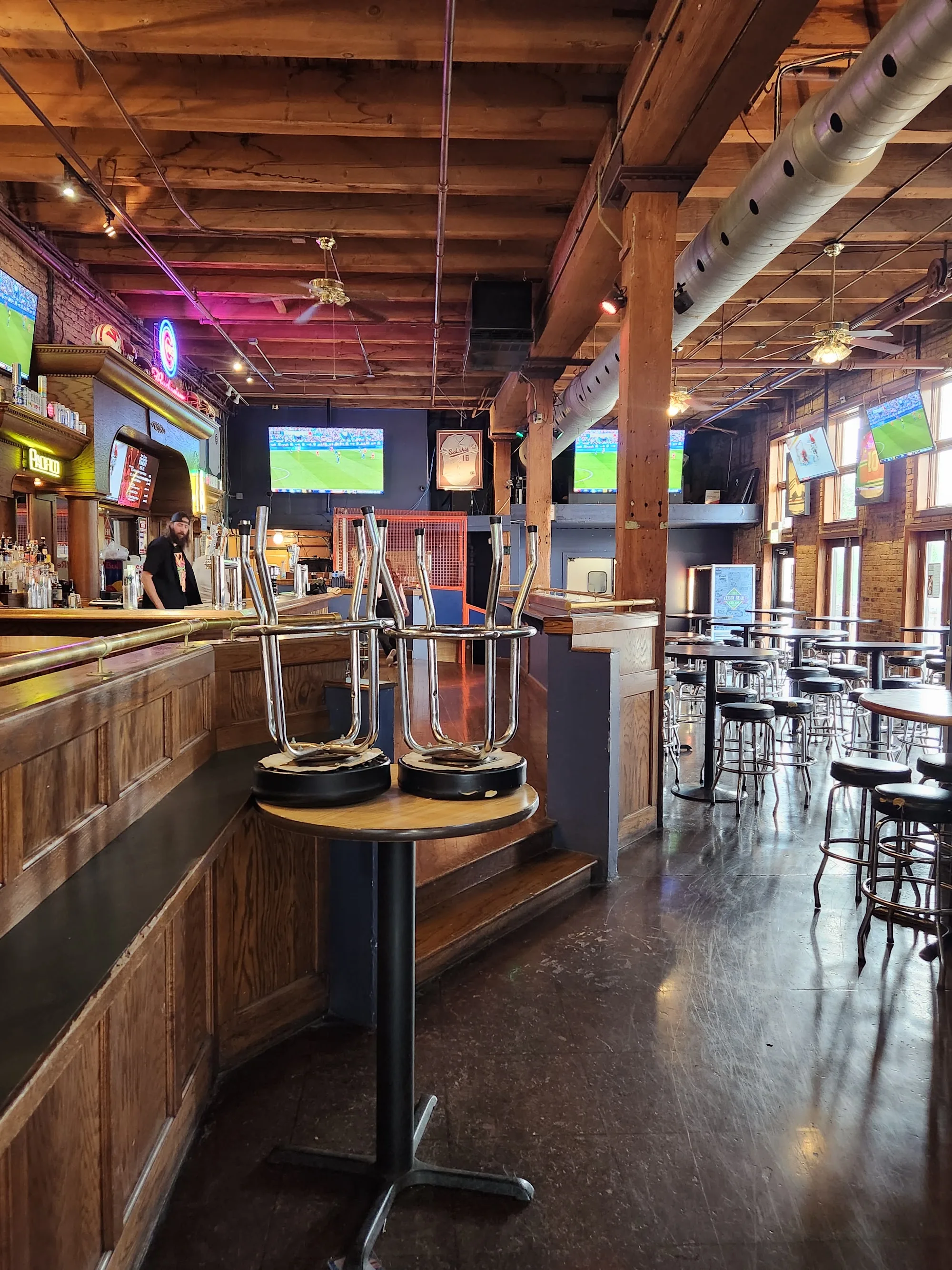 Interior bar area of The Cubby Bear with exposed wood-beam ceiling, high-tops and TVs