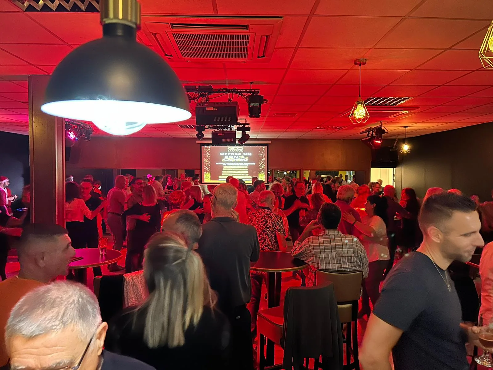 Dance and party event at L'After with people on an illuminated dance floor, red stage lighting and projection screen