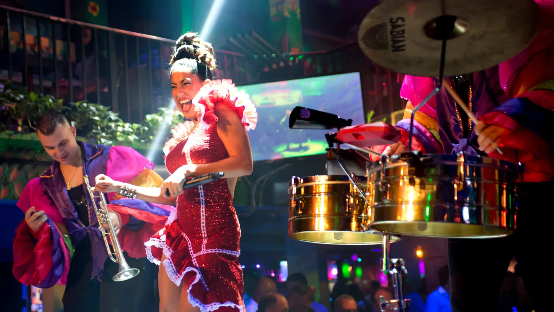 Latin performer in a red ruffle dress dancing beside a trumpeter and percussion during a live show at Mango's Tropical Cafe South Beach in Miami — salsa venue in Miami