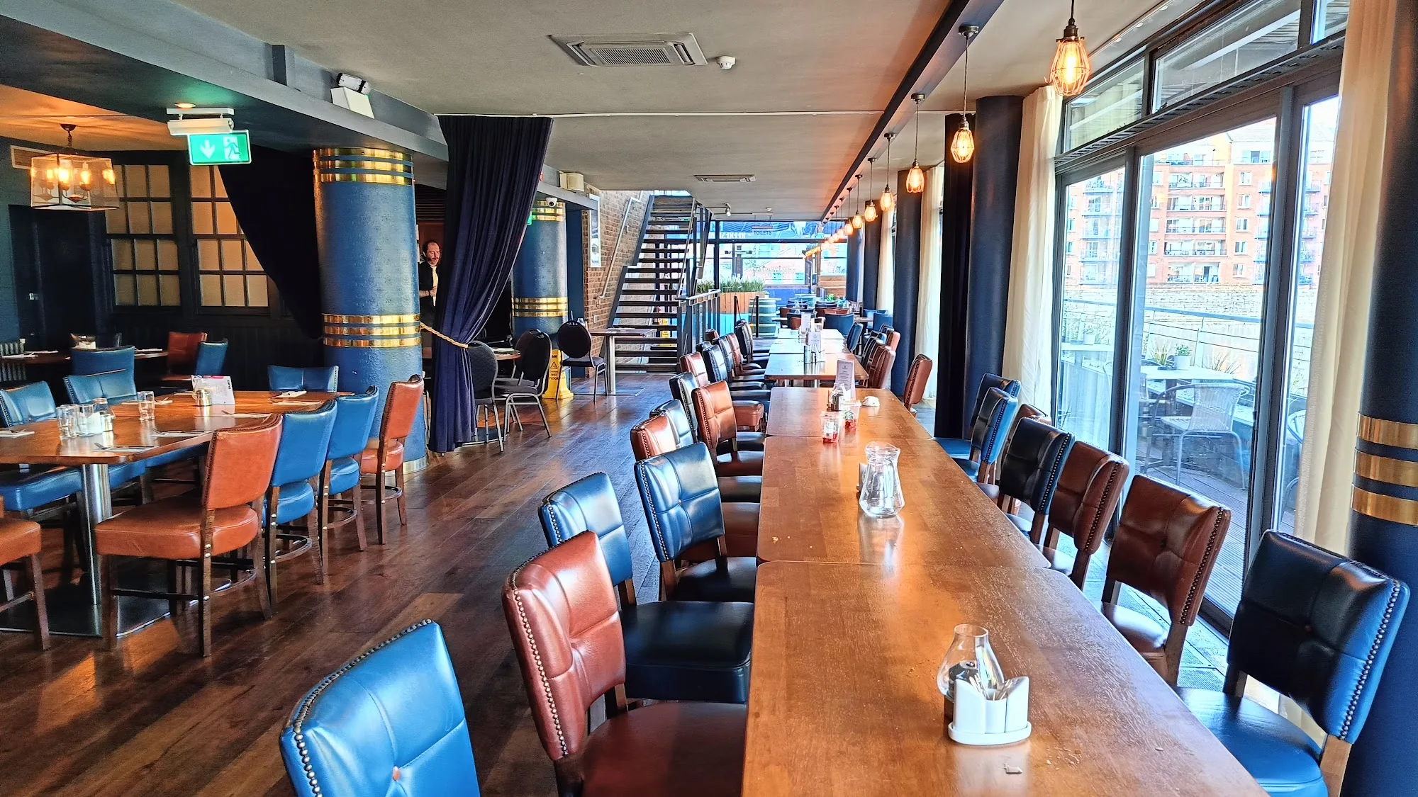 Wide interior of the Harbourmaster Bar in Dublin with a long communal table, blue and red leather chairs and waterfront-facing windows, bachata, salsa venue in Dublin