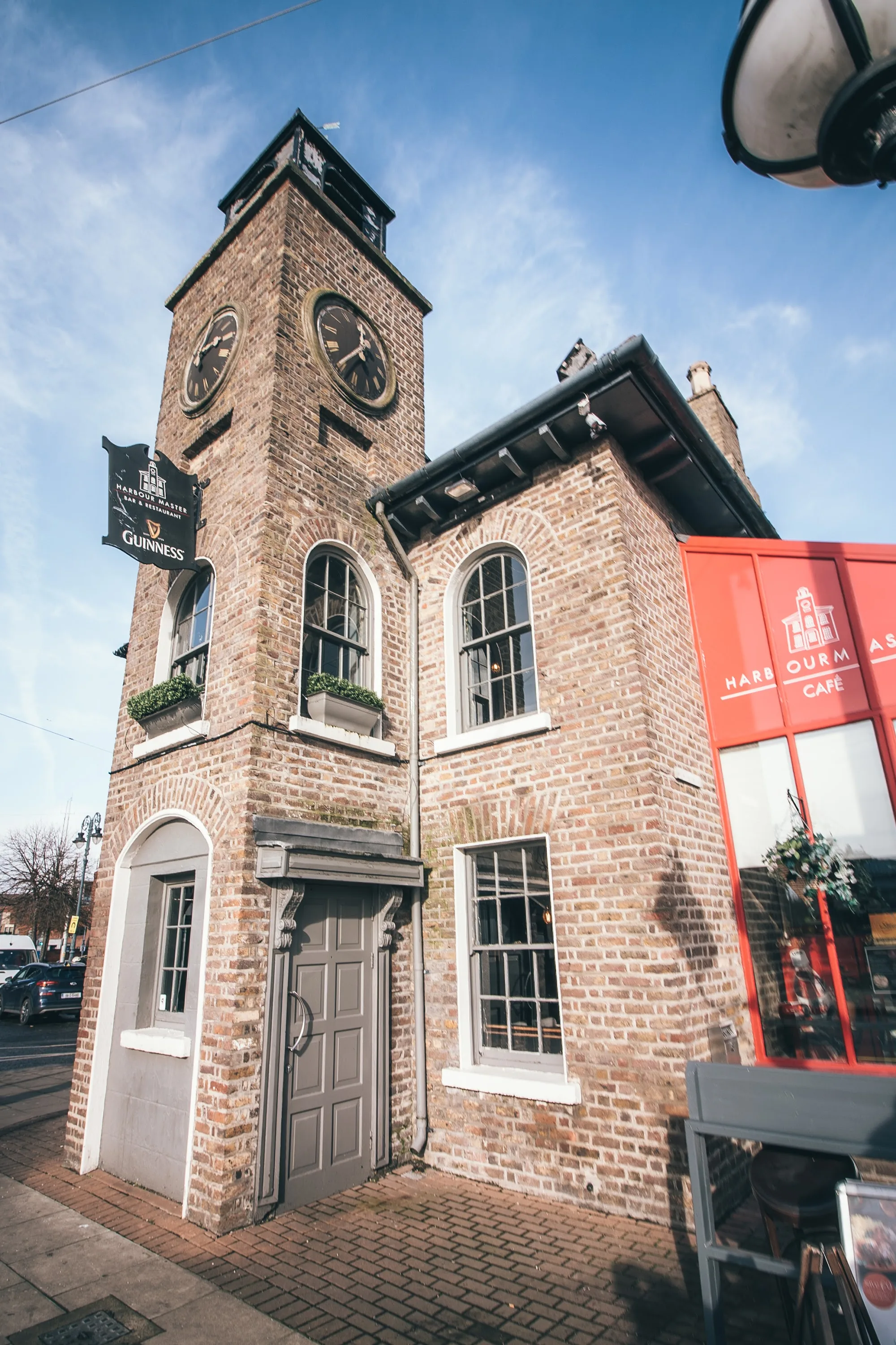 Exterior of the historic Harbourmaster clock tower building in Dublin under a blue sky, with Guinness signage and red cafe branding