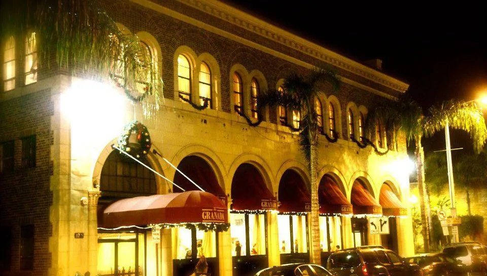 Illuminated arched building facade with red awnings and palm trees at night at The Granada LA, Los Angeles