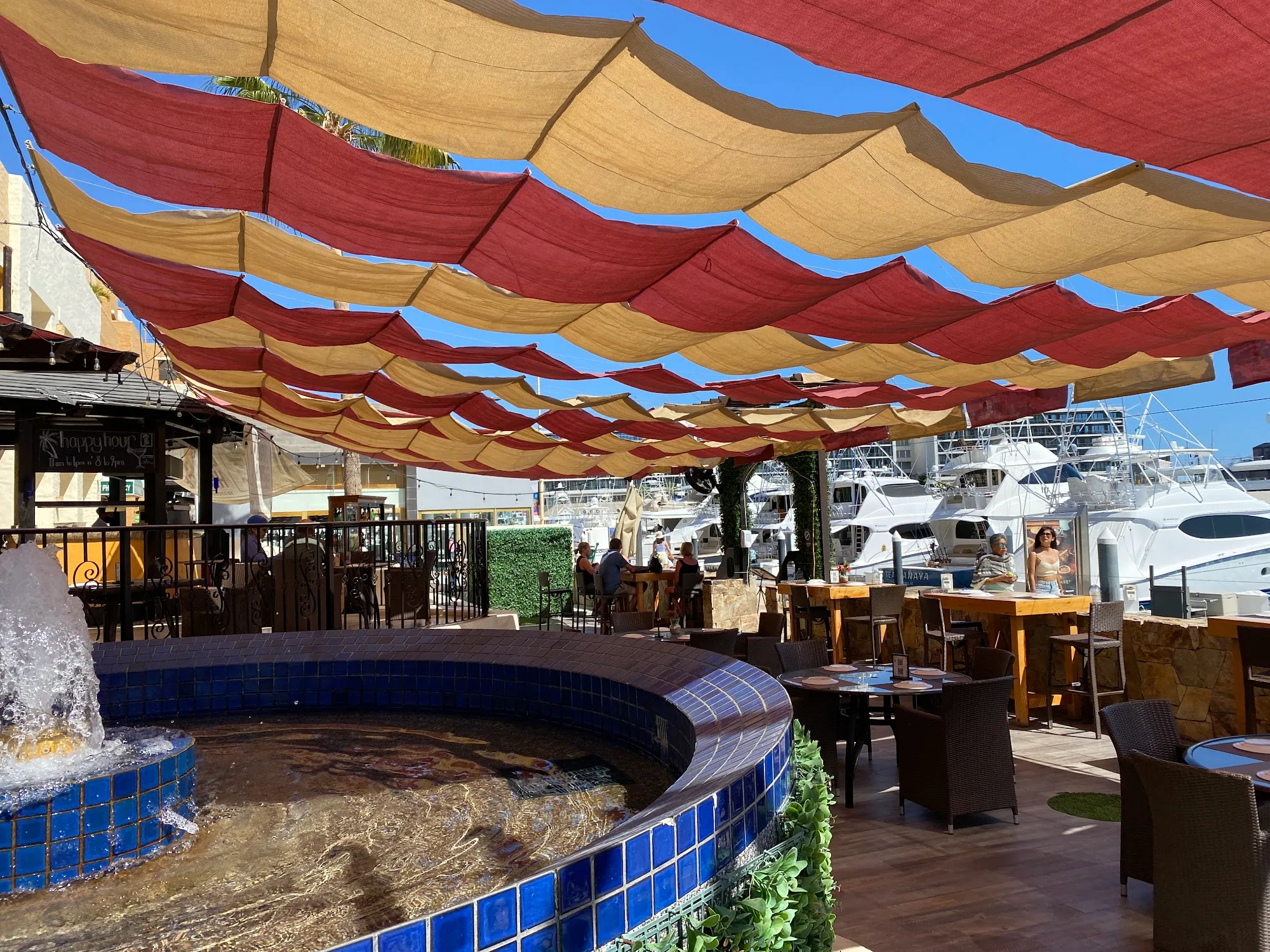 Outdoor terrace at Lighthouse Cabo with red and gold shade sails and marina yacht view