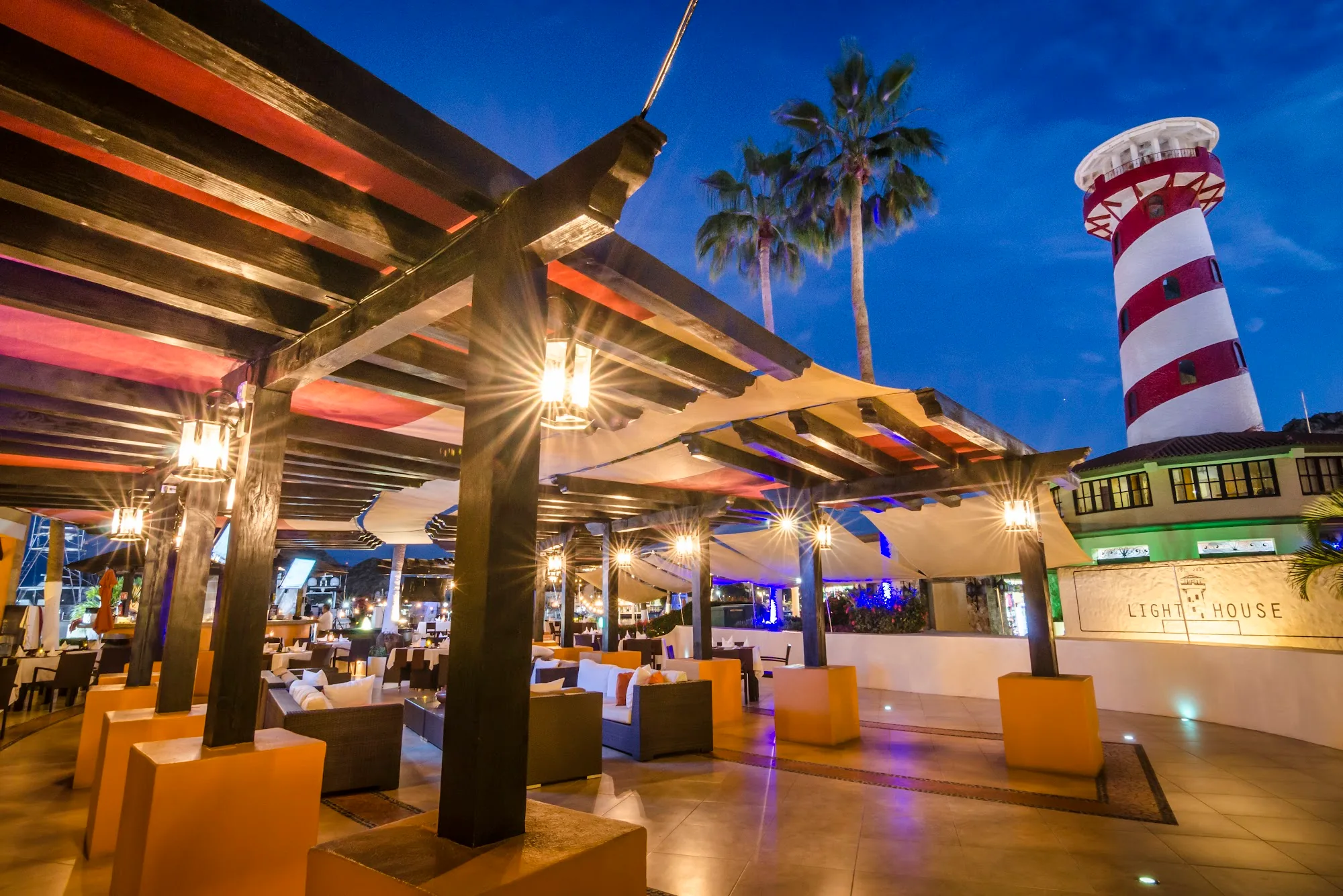 Twilight exterior of Lighthouse Cabo with the iconic red and white striped lighthouse tower and Lighthouse sign lit up