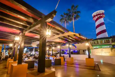 Twilight exterior of Lighthouse Cabo with the iconic red and white striped lighthouse tower and Lighthouse sign lit up — salsa venue in Cabo San Lucas