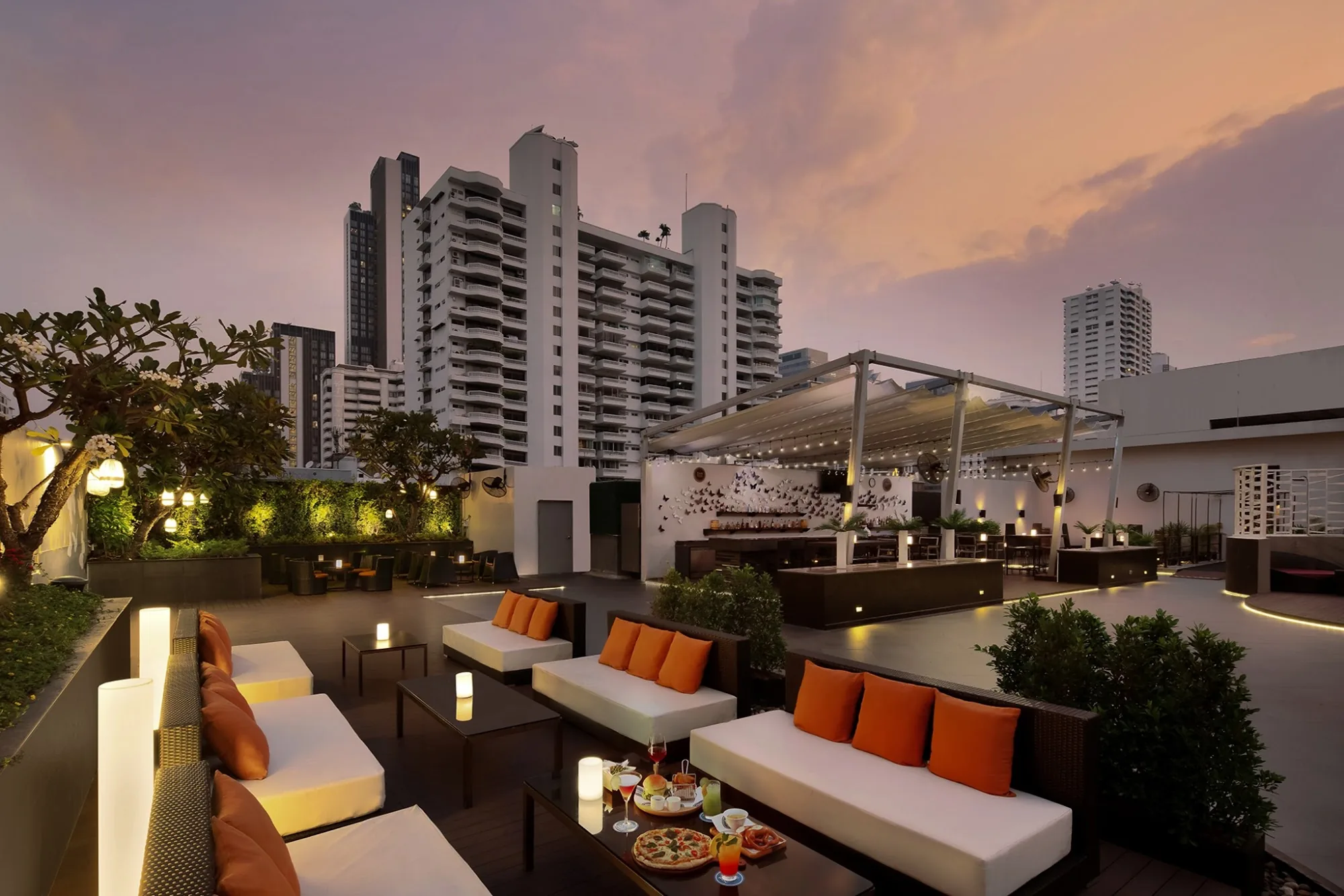Rooftop bar at sunset with orange cushion seating at amBar Sheraton Bangkok