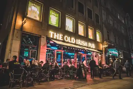 The Old Irish Pub Copenhagen exterior lit up at night with illuminated signage and a busy crowd at outdoor tables, salsa, bachata venue in Copenhagen