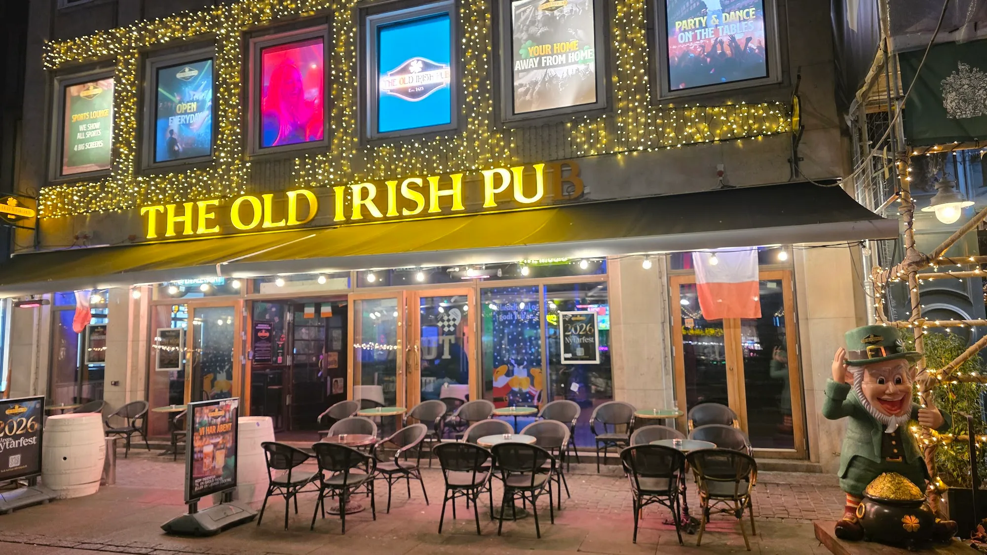 Night view of The Old Irish Pub Copenhagen storefront with glowing signage, string lights and outdoor seating