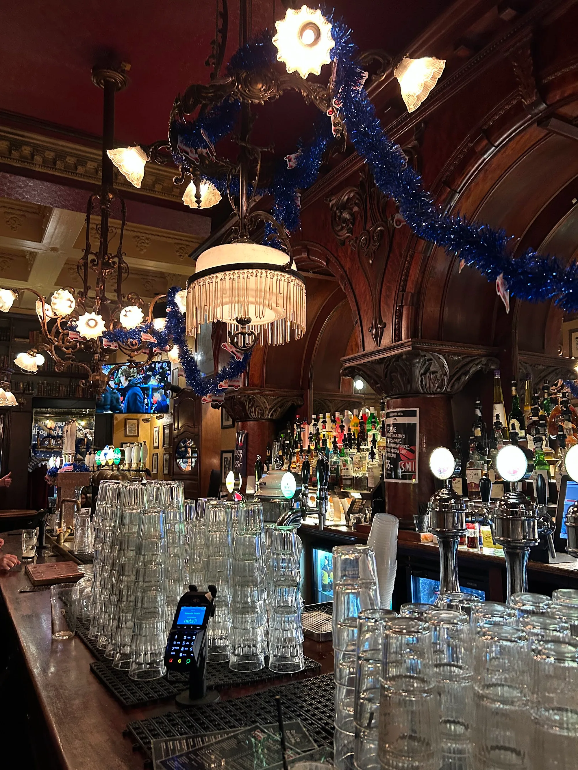 Ornate carved-wood bar interior with chandeliers and detailed lighting inside The Old Irish Pub Copenhagen