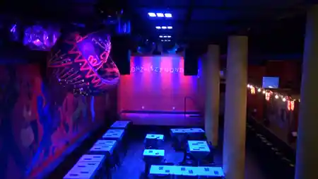 Interior of Gonzalez y Gonzalez dance venue in New York showing the dance floor, stage, and colorful Latin murals under neon lights — salsa, bachata venue in New York