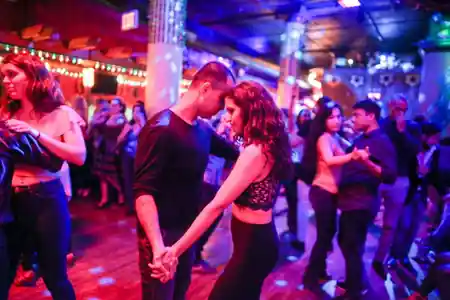 Couple dancing salsa at Gonzalez y Gonzalez in New York with colorful lights and a lively crowd on the dance floor