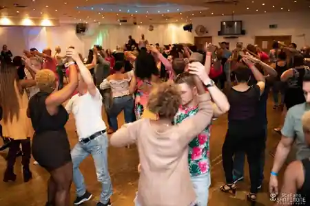 Packed salsa dance floor at Rhythm and Vibes London social, dancers in partner hold during a group class at St John's Angell Town Primary School