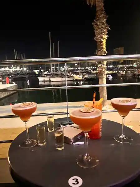 Cocktails on a William Buzz table overlooking the lit-up Alicante marina at night — salsa, bachata, kizomba venue in Alicante