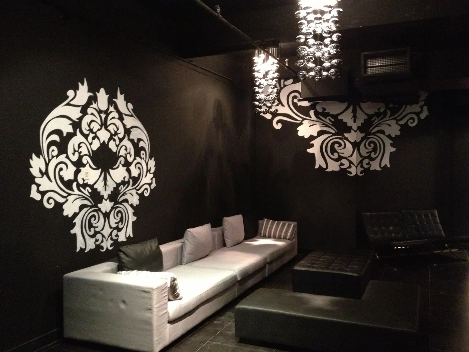 Dark lounge with a long sofa, damask wall art and crystal chandeliers at Espaces des Arts