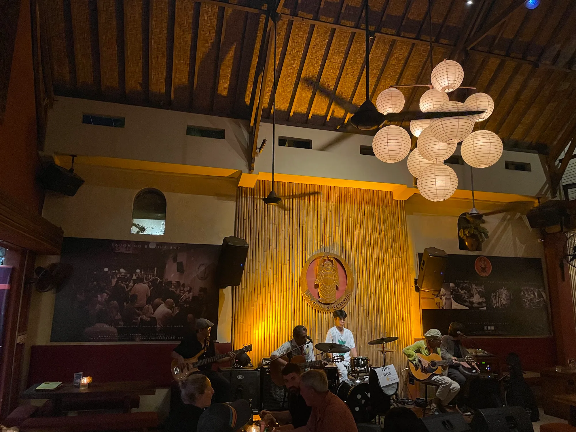 Live band performing on stage at Laughing Buddha Bar in Bali under bamboo backdrop and pendant lights