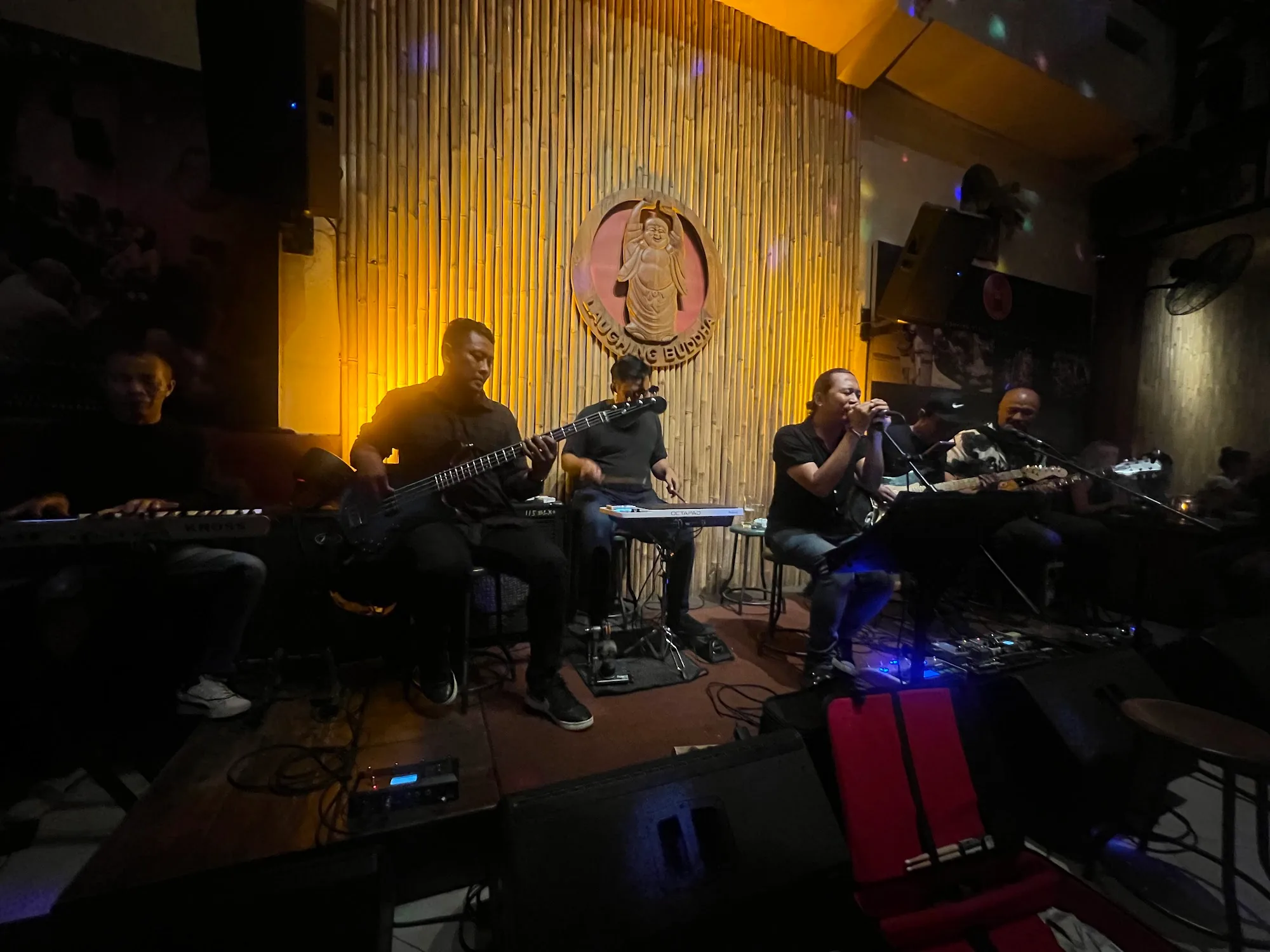 Live band on stage at Laughing Buddha Bar Bali with branded backdrop and colorful disco lighting