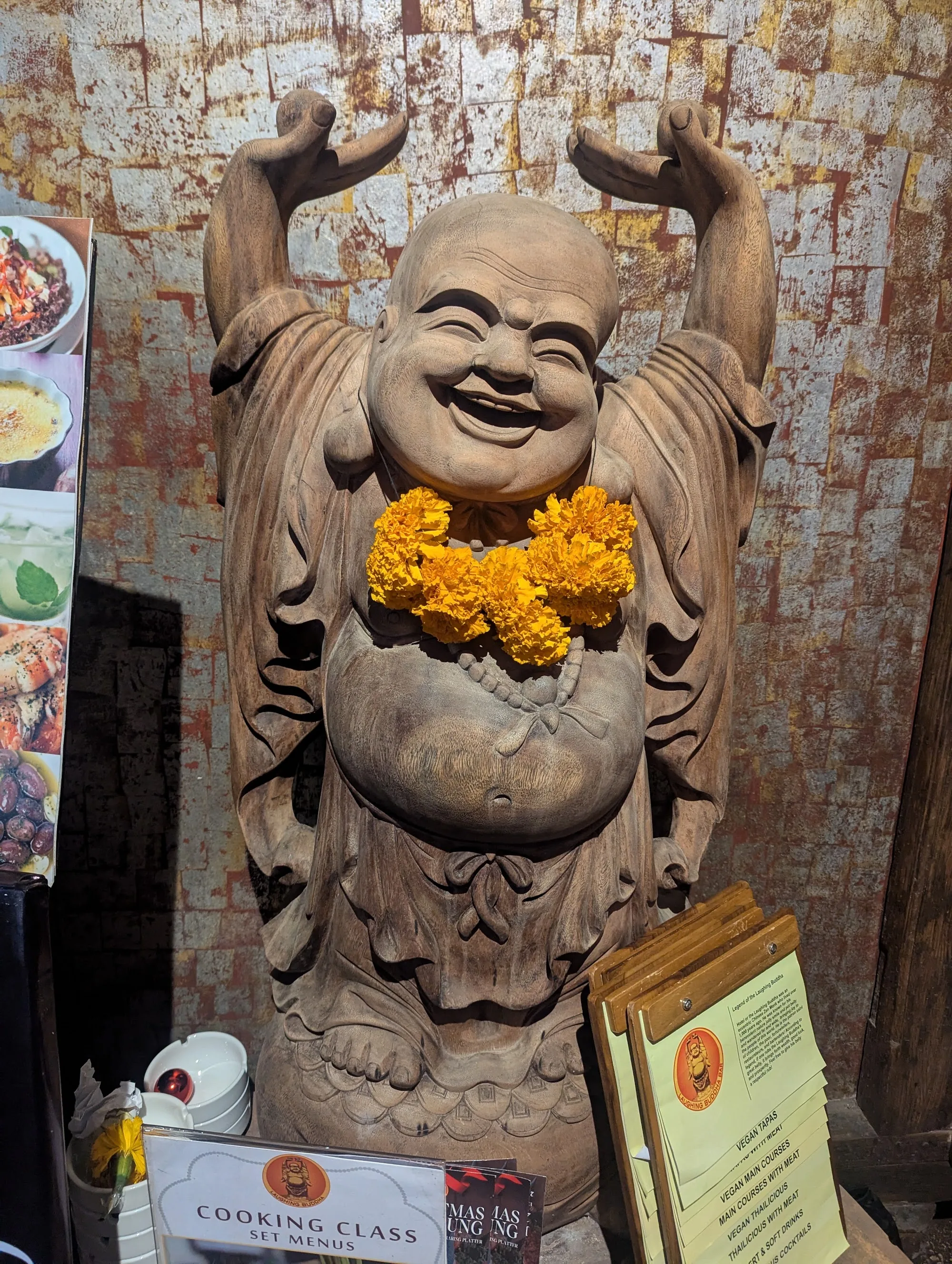Carved Laughing Buddha statue with marigold garland inside the entrance of Laughing Buddha Bar Bali