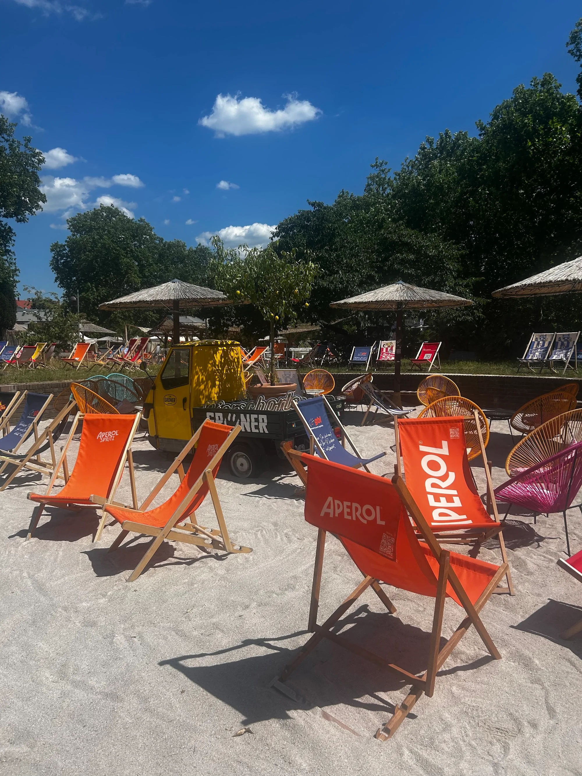 Colorful Aperol-branded deckchairs on sandy beach at Lieblingsstrand with parasols and a tuk-tuk bar