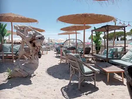 Beach club setting at Le Vieux Rocher with driftwood sculpture, thatched parasols and sand — kizomba, bachata, salsa venue in Golfe Juan