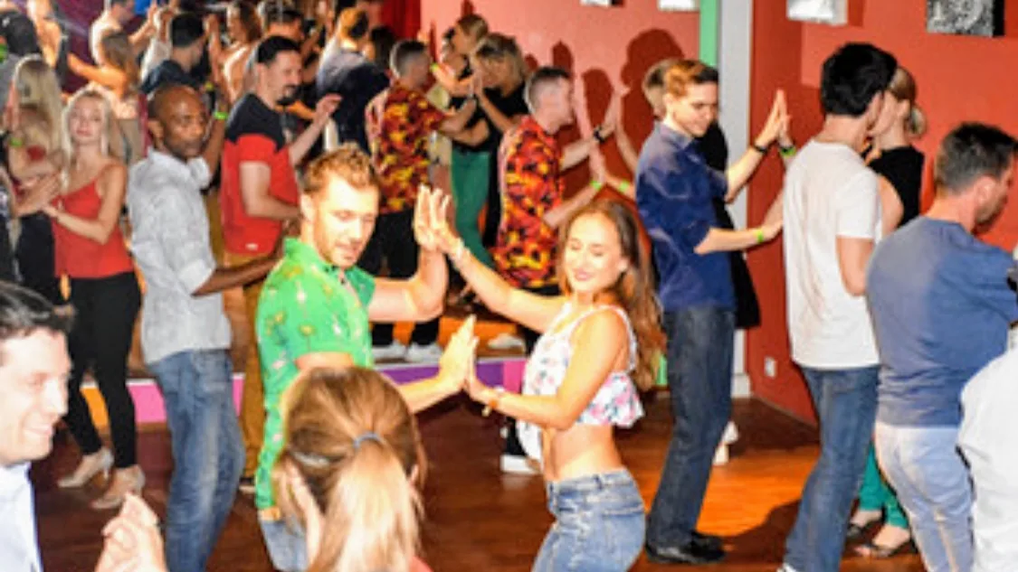 Dancers partnering with hands raised on the dance floor at The Embassy Room Brussels, colorful walls and party crowd, kizomba venue in Brussels