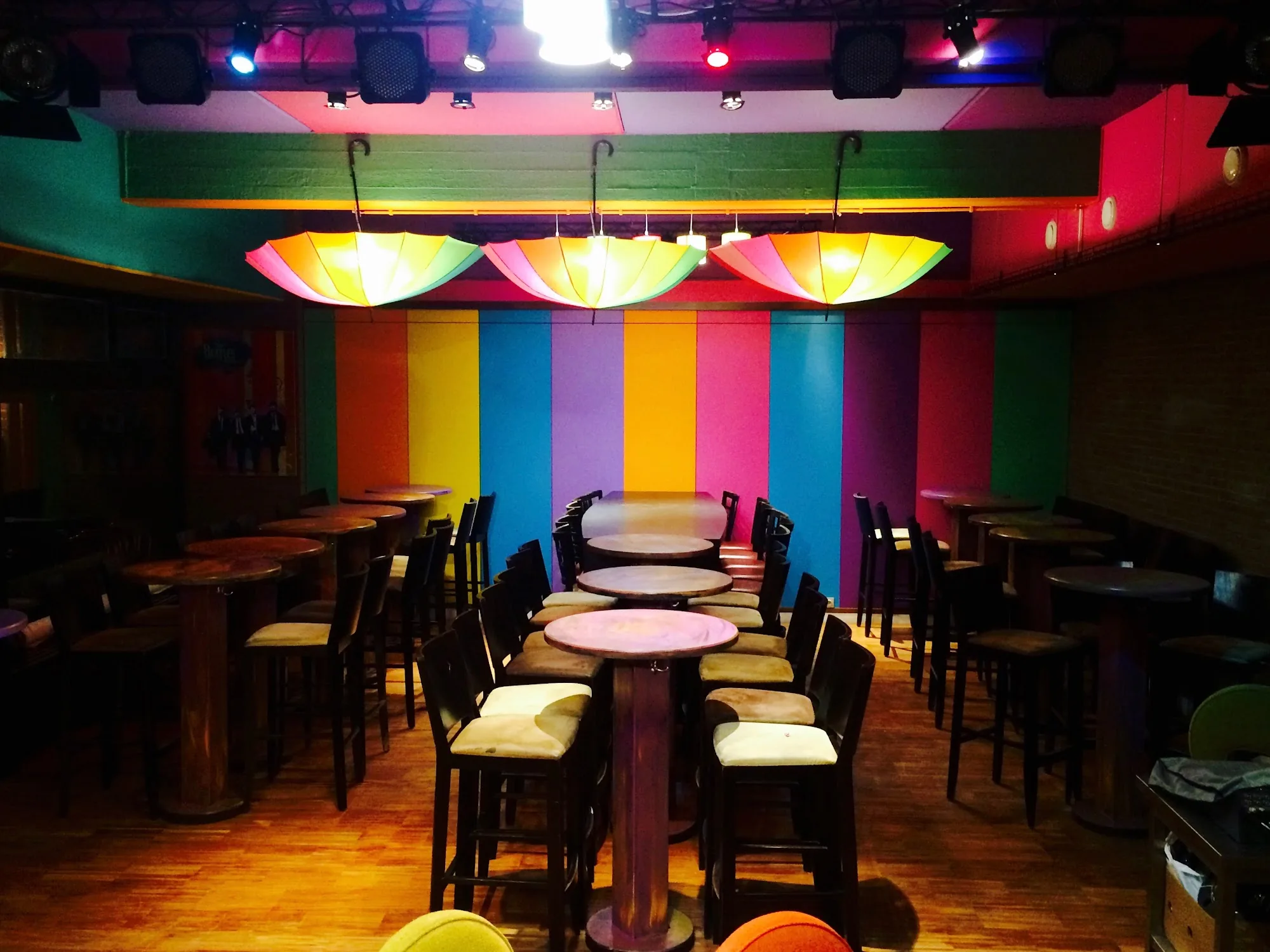 Colorful club interior at The Embassy Room Brussels with rainbow walls, umbrella lights and stage lighting rig above bar seating
