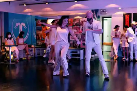 Salsa couple performing an elegant routine in matching white outfits at a social dance event at 8th Floor Fung Woo Centre in Hong Kong, with fellow dancers watching