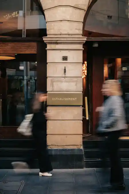 Pedestrians pass the sandstone Establishment Bar entrance with signage on George Street Sydney — salsa, bachata, merengue venue in Sydney
