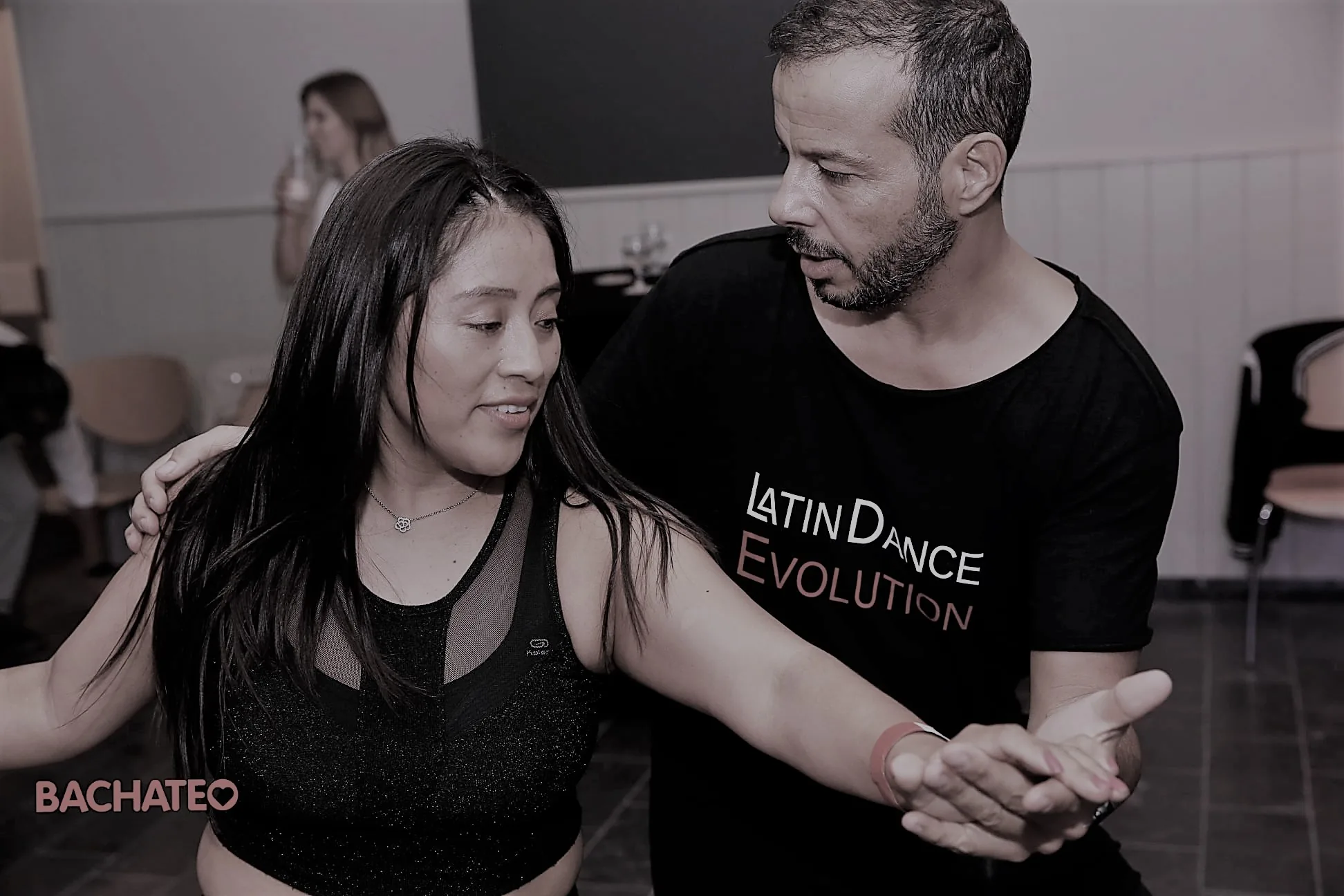 Couple dancing bachata at a Latin Dance Evolution social in Brussels, one wearing a Latin Dance Evolution shirt