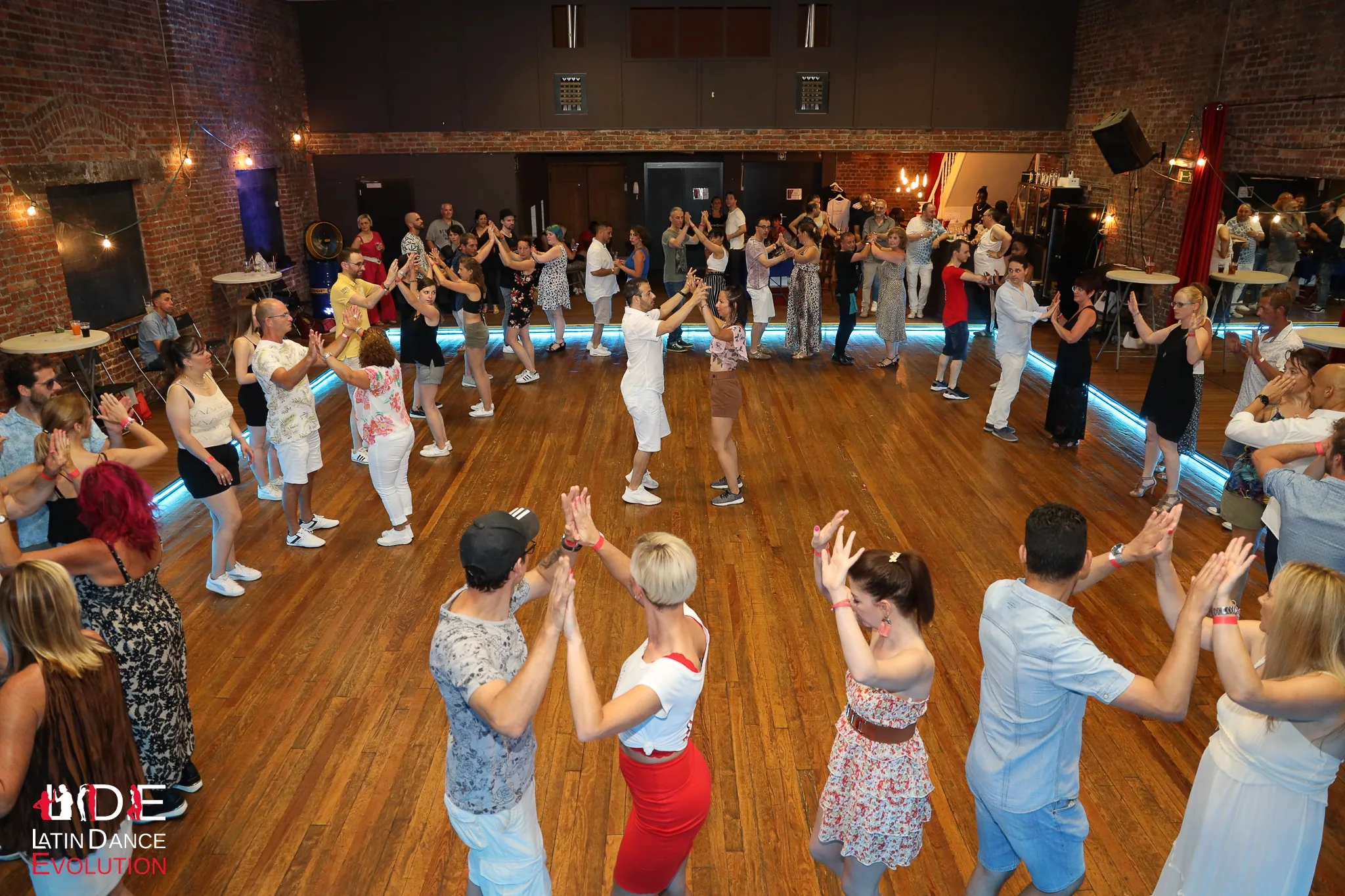 Dancers in a large circle during a Latin Dance Evolution social in a brick-walled Brussels hall, bachata, salsa venue in Brussels