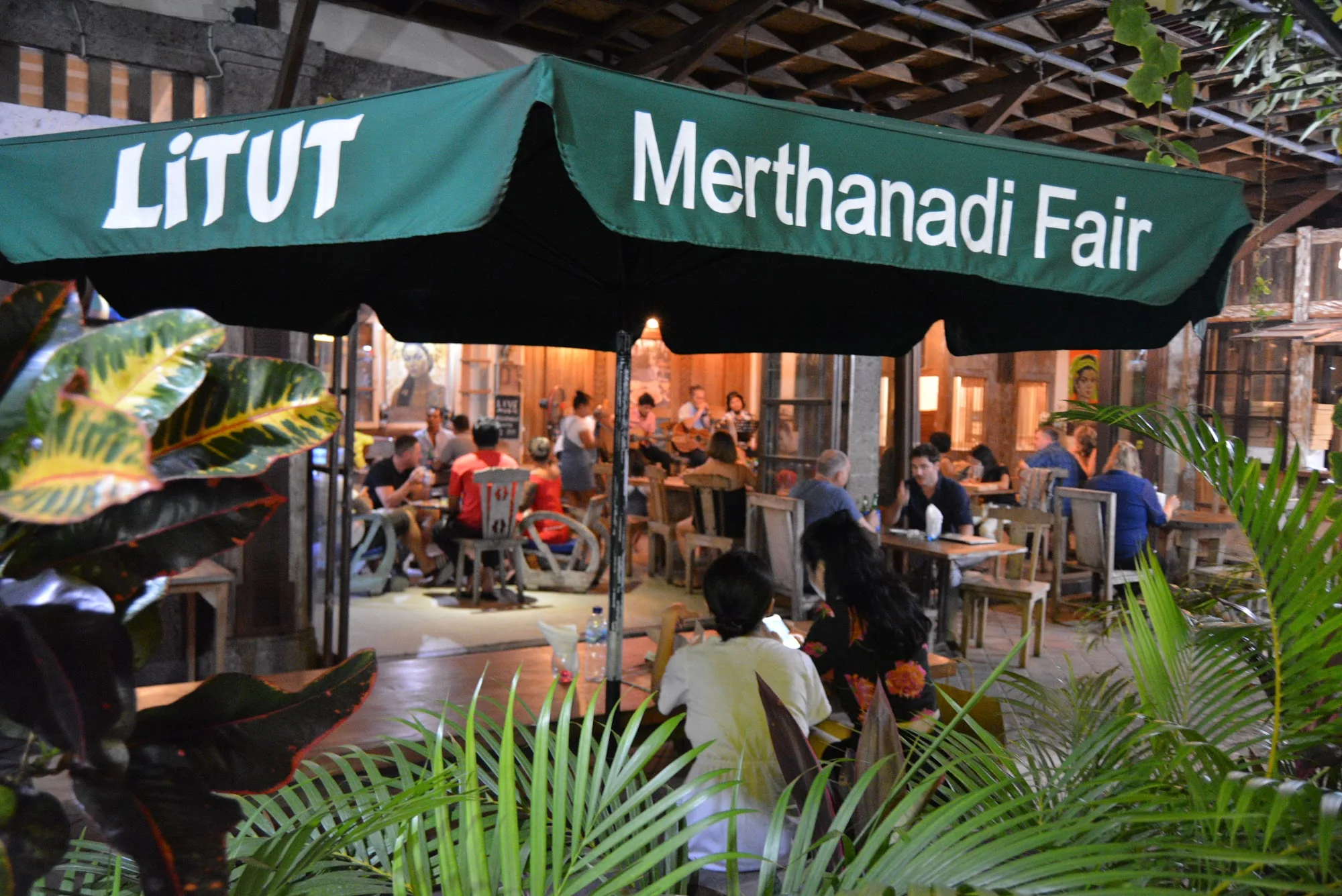 Branded LITUT umbrella over open-air seating with guests at Litut Bar & Restaurant in Bali