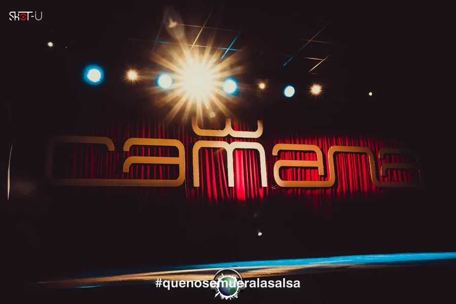 Illuminated Camana stage sign with red curtain backdrop at Camana Club Milan
