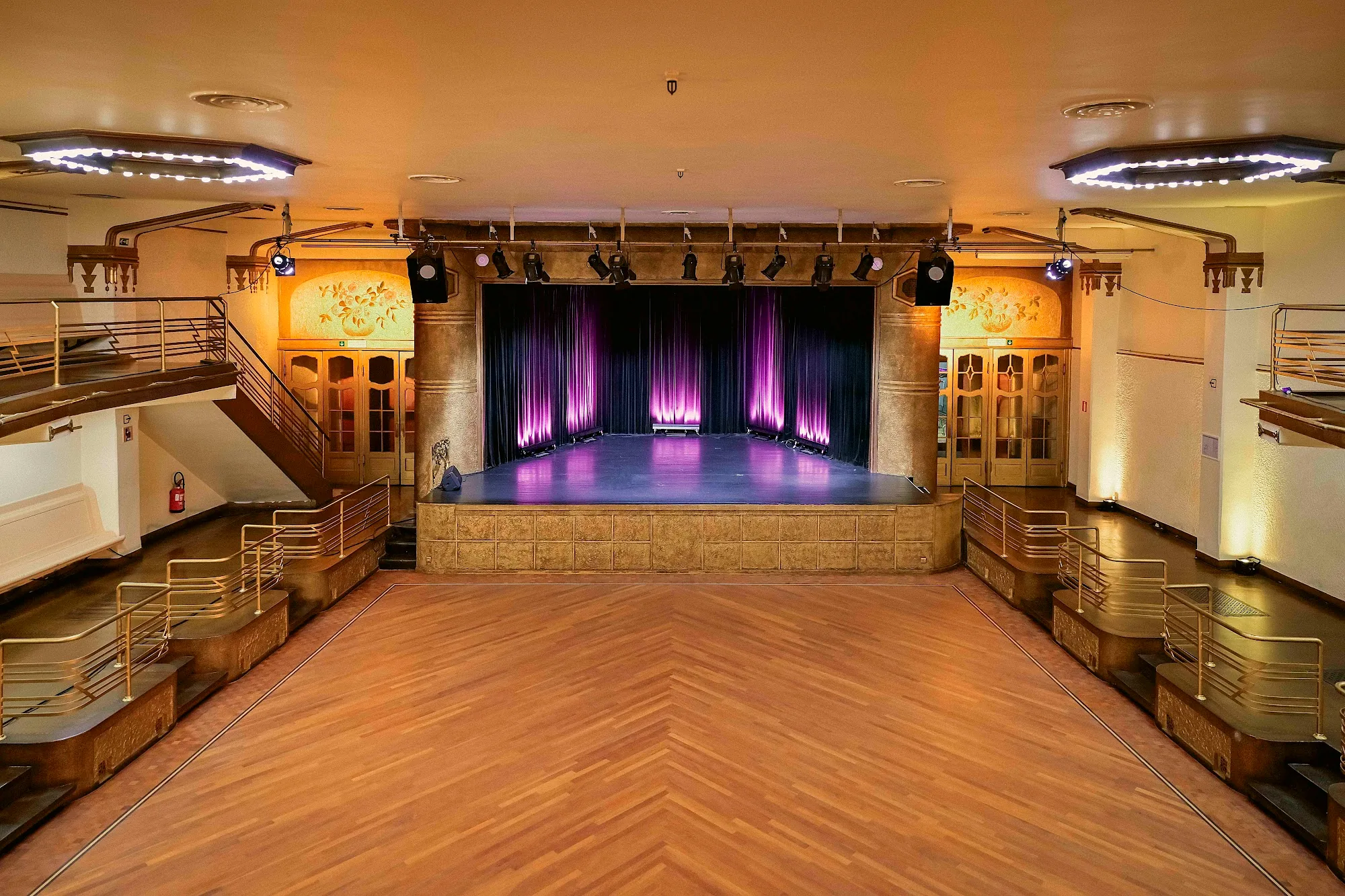 Wide herringbone wooden dance floor facing a purple-lit stage framed by art nouveau columns at Albert Hall Brussels