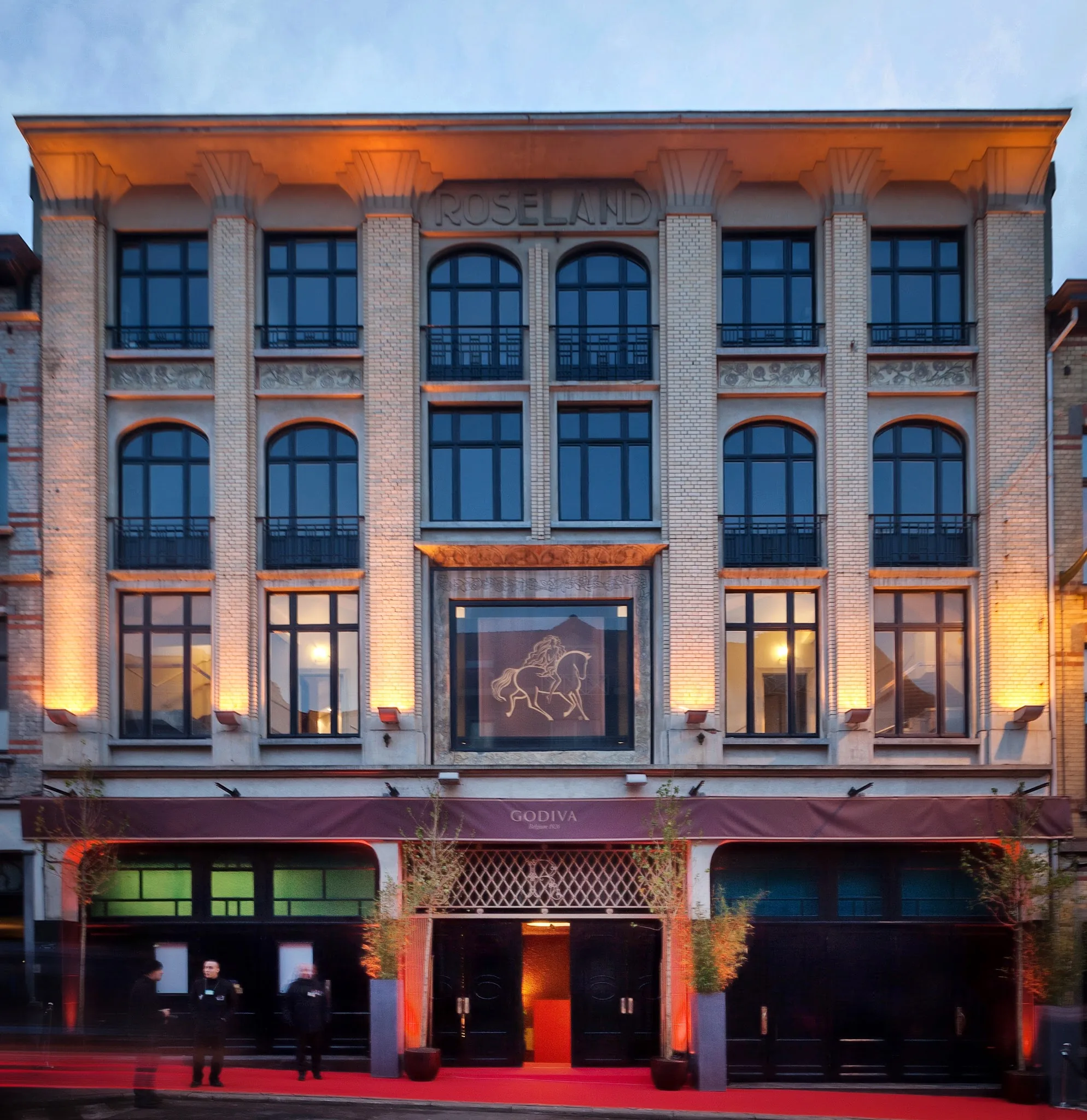 Illuminated Roseland facade of Albert Hall Brussels at dusk with a red carpet entrance and warm lit windows