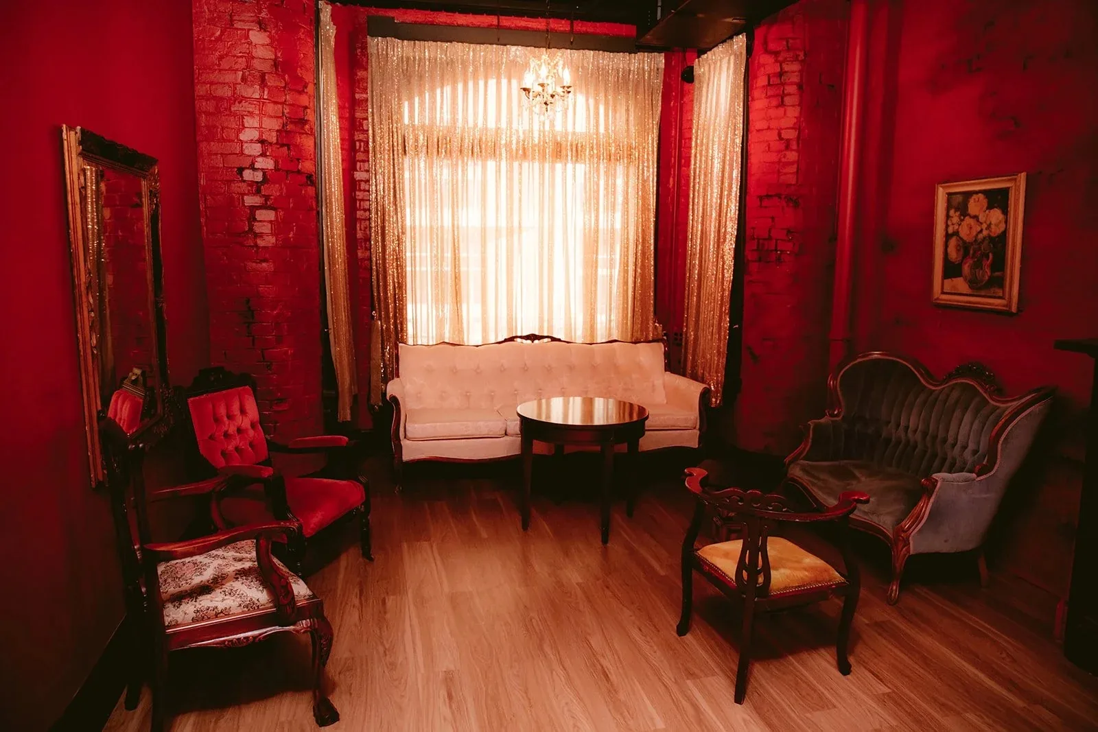 Red-walled room with a cream tufted sofa, gray and red velvet Victorian chairs, gold sequin curtains and exposed brick at Eighteenth Street Lounge, Washington.